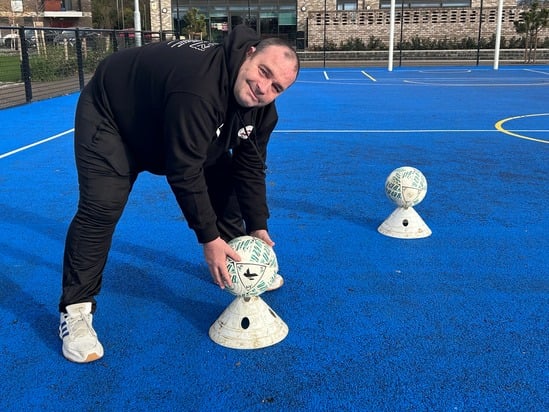 Person on a blue sports court with balls on stands